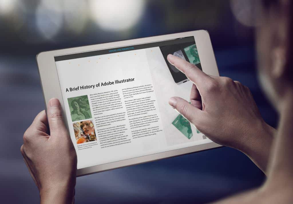 This is a photograph of a reader using a tablet to read 'A Brief History of Adobe Illustrator', a publication Adobe created to showcase it's company history.