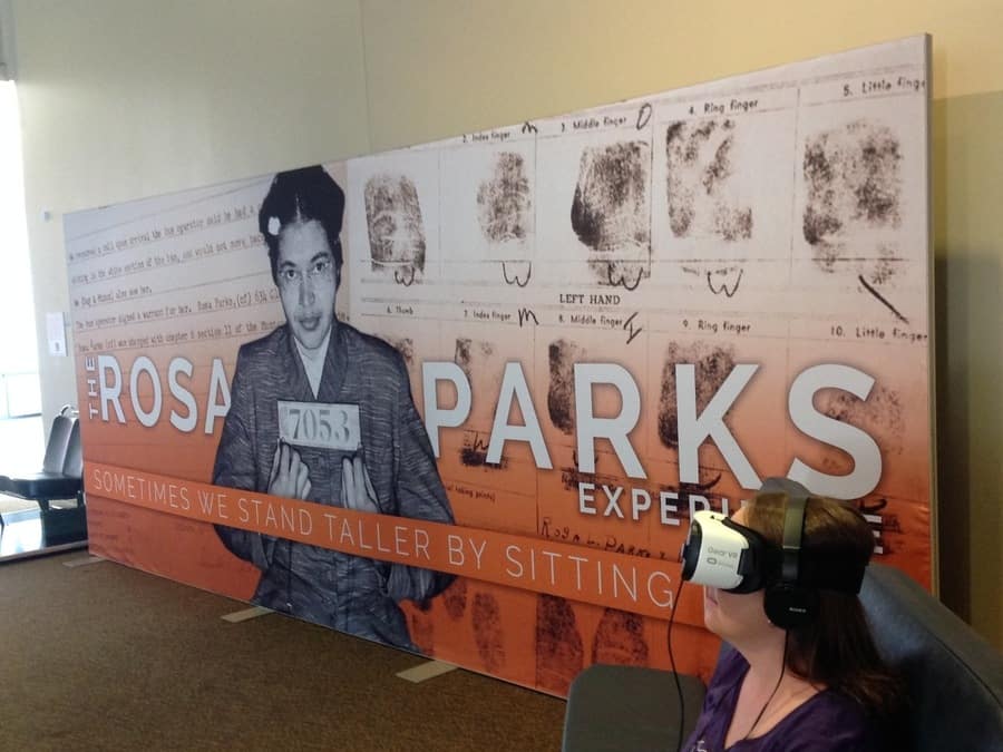 This is a photograph of The Rosa Parks Experience exhibit, which uses virtual reality to show participants what it was like while Rosa Parks lived and what she experienced. A participant is wearing a VR headset.
