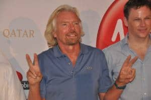 This is a photograph of Richard Branson, founder of the Virgin Group, posing with his hands showing the peace sign.
