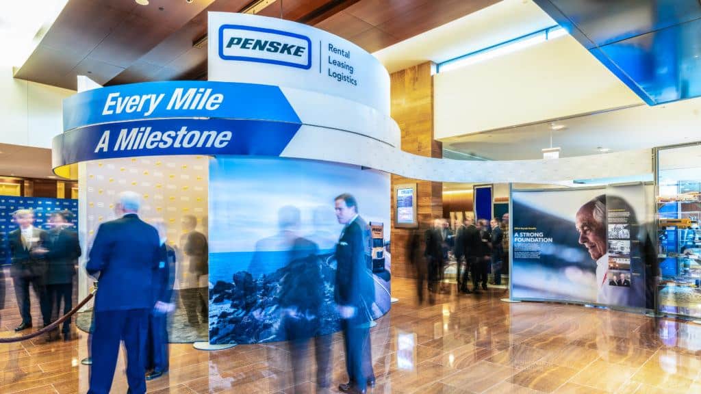 This is a timelapse photo of the custom exhibit Penske created to showcase their company history. Visitors can clearly see their tagline, which is 'Every Mile a Milestone'.